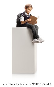 Schoolboy sitting on a tall white column and reading a book isolated on white background - Shutterstock ID 2184459547
