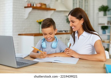 Schoolboy sitting at table and writing in copybook on online lesson. Smiling mom helping her son doing homework studying online using laptop in home kitchen. Online education, remote learning concept. - Powered by Shutterstock