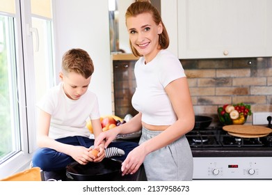 Schoolboy Son Helping Mom In The Kitchen To Cook Breakfast Holding A Chicken Egg In His Hands Mom Smiling Happy Family Lonely Mother