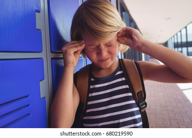 Schoolboy suffering from headache while standing by lockers in corridor at school - Powered by Shutterstock