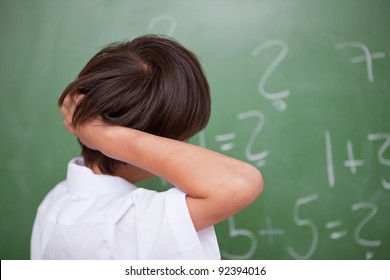 Schoolboy Thinking While Scratching The Back Of His Head In Front Of A Chalkboard