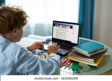 Schoolboy Is Typing Report On Laptop, Do Homework. Caucasian Teen Boy Engaged In E-learning, Looks At Screen Of Laptop