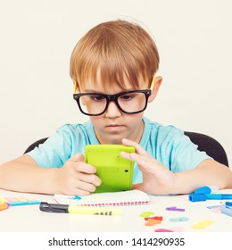 Schoolboy Wearing Eyeglasses Studying. Little Boy Does Homework. Kid Using Calculator, Sits At Table. Elementary School And Education.