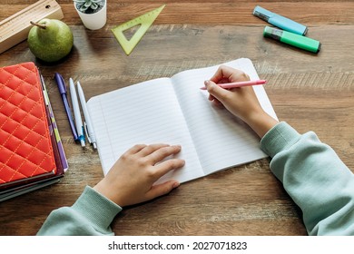 Schoolchild  writing in a notebook at home at his desk.Completing homework.Stationery, textbooks and notebooks are on the table.Back to school concept.Top view, copy space.