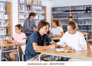 Schoolchildren studying in the school library write down a summary from a textbook in a exercise book, discussing topical ..issues