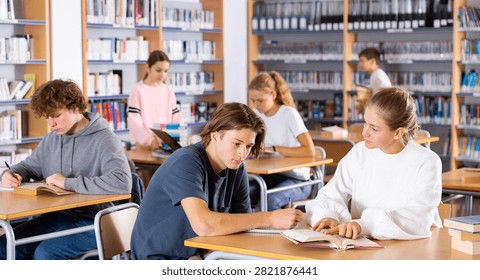 Schoolchildren studying in the school library write down a summary from a textbook in a exercise book, discussing topical ..issues