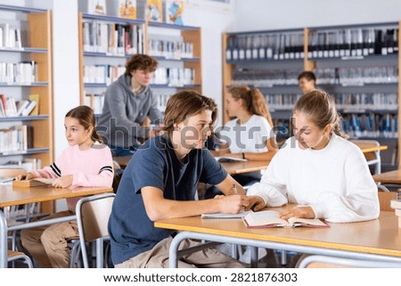 Schoolchildren studying in the school library write down a summary from a textbook in a exercise book, discussing topical ..issues