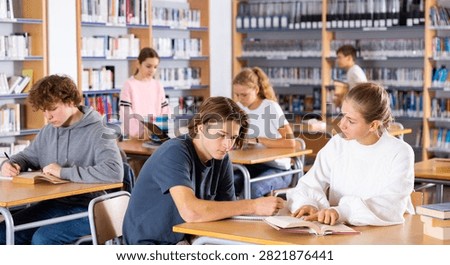 Schoolchildren studying in the school library write down a summary from a textbook in a exercise book, discussing topical ..issues