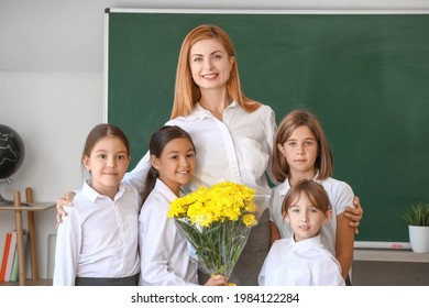 Schoolchildren with teacher and bouquet of flowers in classroom