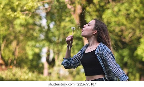 Schoolgirl blows a dandelion on a summer day.
