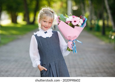 Schoolgirl with a bouquet of flowers at the start of the school year in uniform in a city park. The first time in first class.
