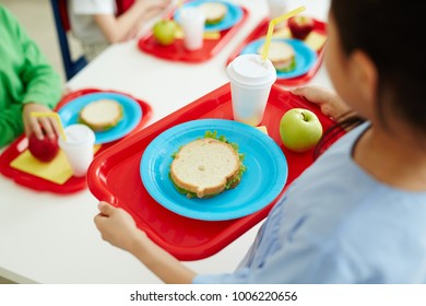 Schoolgirl Carrying Red Plastic Tray With Sandwich On Plate, Glass Of Drink And Green Apple During Lunch Break