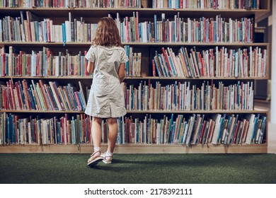 Schoolgirl choosing book in school library. Smart girl selecting literature for reading. Books on shelves in bookstore. Learning from books. School education. Benefits of everyday reading - Powered by Shutterstock