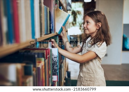 Schoolgirl choosing book in school library. Smart girl selecting literature for reading. Books on shelves in bookstore. Learning from books. School education. Child curiosity. Back to school