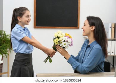 Schoolgirl congratulating her pedagogue with bouquet in classroom. Teacher's day - Powered by Shutterstock