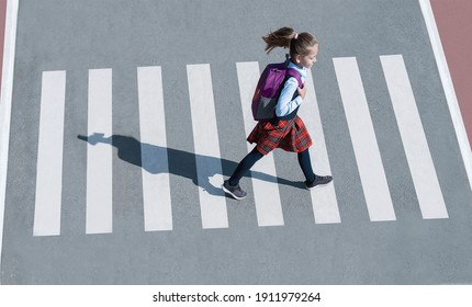 Schoolgirl crossing road on way to school. Zebra traffic walk way in the city. Concept pedestrians passing a crosswalk.  Stylish young teen girl walking with backpack. Active child. Top view