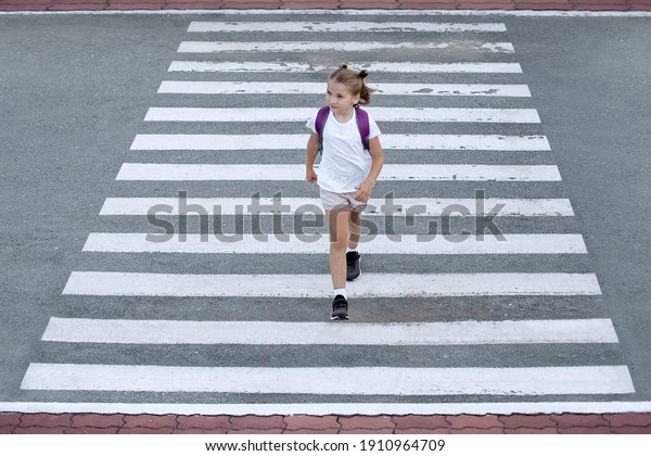 Schoolgirl\
crossing road on way to school. Zebra traffic walk way in the city.\
Concept pedestrians passing a crosswalk.  Stylish young teen girl\
walking with backpack. Active child. Top\
view