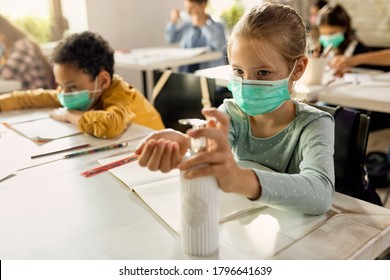 Schoolgirl with face mask using hands sanitizer while sitting at a desk in the classroom. - Powered by Shutterstock