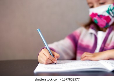 Schoolgirl girl in mask studying homework at home, social distance during quarantine coronavirus