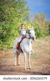 Schoolgirl Girl Rides A White Pony. The Child Is Riding A Horse. Horse Riding Training For Children. Controlling The Horse With The Reins