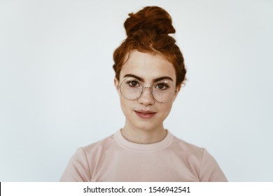 a schoolgirl with glasses, with a smart look, stands in a light-colored studio