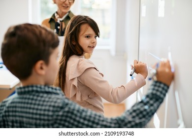 Schoolgirl And Her Classmate Writing On Interactive Screen On Smartboard At Elementary School. 