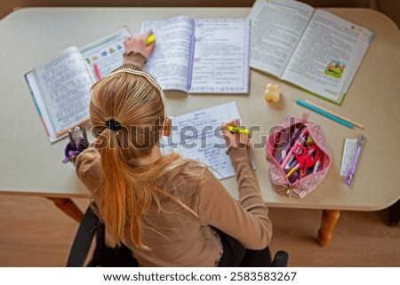 Schoolgirl highlighting notes while studying, A girl at a desk highlighting important points in her homework surrounded by books and stationery. Top view