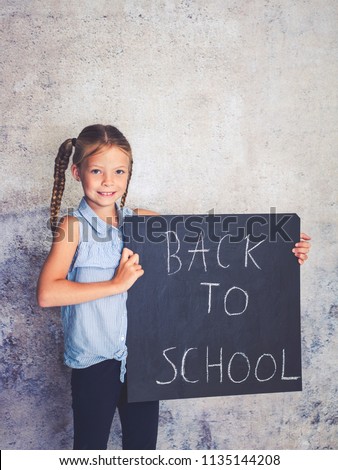schoolgirl is holding blackboard with the words back to school in front of concrete background