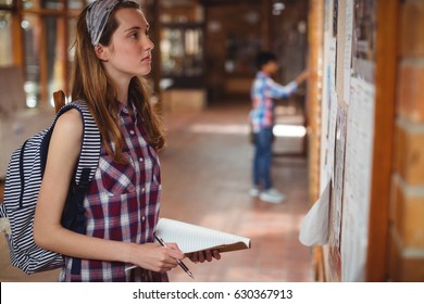 Schoolgirl reading notice board in corridor at school - Powered by Shutterstock