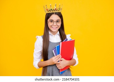 Schoolgirl in school uniform and crown celebrating victory on yellow background. School child hold books. Education graduation, victory and success. Happy teenager school girl.