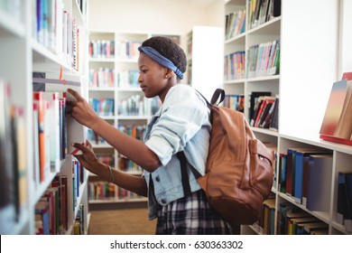 Schoolgirl selecting book from book shelf in library at school - Shutterstock ID 630363302