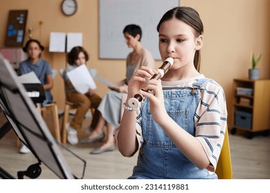 Schoolgirl sitting in front of sheet music and learning to play flute in music class