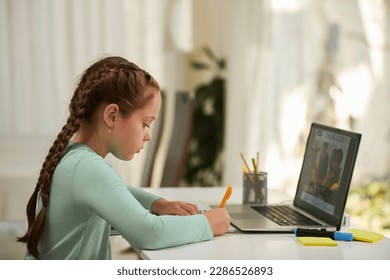 Schoolgirl taking notes in textbook when watching educational video on school platform - Powered by Shutterstock