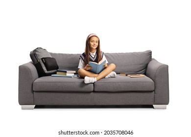 Schoolgirl in a uniform sitting on a couch and reading a book isolated on white background