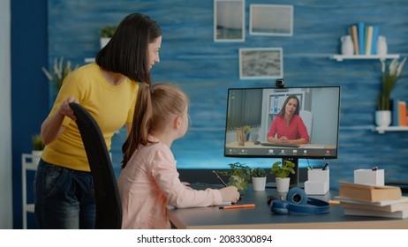 Schoolgirl Using Video Call For Online Lesson With Teacher And Mother At Home. Parent Giving Assistance To Young Child While Attending School Courses With Video Conference On Computer.