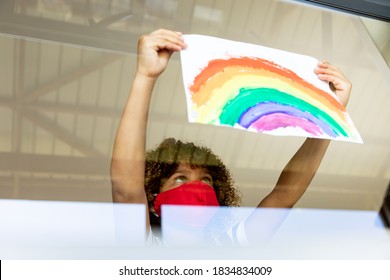 Schoolgirl wearing face mask, glueing a rainbow drawing to a window. Education back to school health safety during Covid19 Coronavirus pandemic. - Powered by Shutterstock