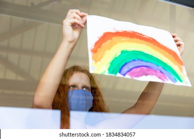 Schoolgirl wearing face mask, glueing a rainbow drawing to a window. Education back to school health safety during Covid19 Coronavirus pandemic. - Powered by Shutterstock