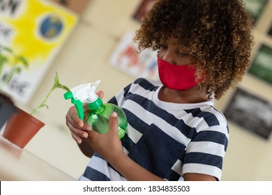 Schoolgirl wearing face mask, watering a plant in a class. Education back to school health safety during Covid19 Coronavirus pandemic. - Powered by Shutterstock