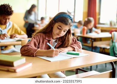 Schoolgirl writing while learning during a class in the classroom. - Powered by Shutterstock