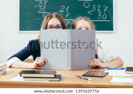 Schoolgirls hiding behind book sitting in a classroom