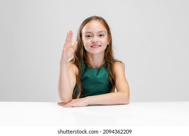 Schooling. Portrait of studious pupil, girl raising hand to answer isolated over white background. Concept of childhood, family, happiness, education, emotions, facial expression. Copy space for ad