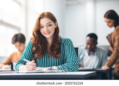 School's in Session. Portrait of happy red haired female student sitting at table in academic auditorium, posing and looking at camera. Higher educational institutions, learning with pleasure
