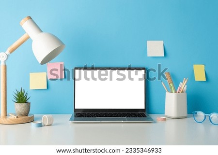 School-themed setup: side view photo of desk furnished with stationery holder, glasses, flowerpot on blue wall background with sticky notes. Empty laptop screen offers perfect space for text or ads