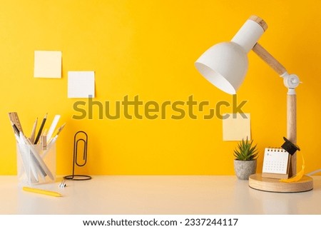 Schooltime creativity arrangement. Side view photo of pencil stand, ruler, clip shaped book holder, calendar, tiny academic hat, plant, lamp, sticky notes, yellow wall background. Space for text or ad
