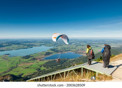 Schwangau, Germany - October 11, 2017: Elevated view of the jump ramp for paraglider pilots on the Tegelberg in Bavaria with just launched planes and athletes looking to jump behind under blue sky.
