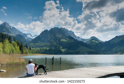 Schwarzsee, FR / Switzerland - 1 June 2019: woman tourist and pet dog enjoy the summer lakeside view at the Schwarzsee Lake in the Swiss Alps in canton Fribourg