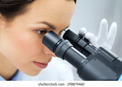 science, chemistry, technology, biology and people concept - close up of young female scientist face looking to microscope eyepiece and making or research in clinical laboratory - Powered by Shutterstock