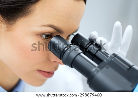 science, chemistry, technology, biology and people concept - close up of young female scientist face looking to microscope eyepiece and making or research in clinical laboratory
