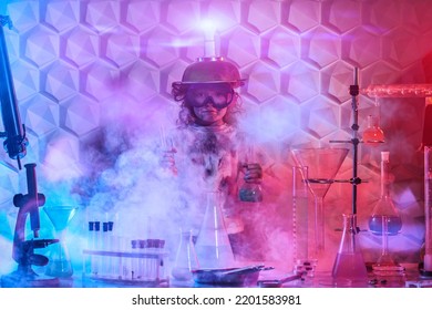 Science Experiments And Children. An Upset Little Girl With Goggles And A Strange Invention On Her Head  Stands With Flasks In The Chemical Laboratory After Failed Experiments. Education.