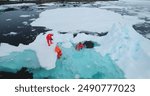 Science exploration on South Pole. People explore global warming in Antarctica. Group of scientists in orange wetsuits take samples and measure melting glacier water, climate change problem. Aerial